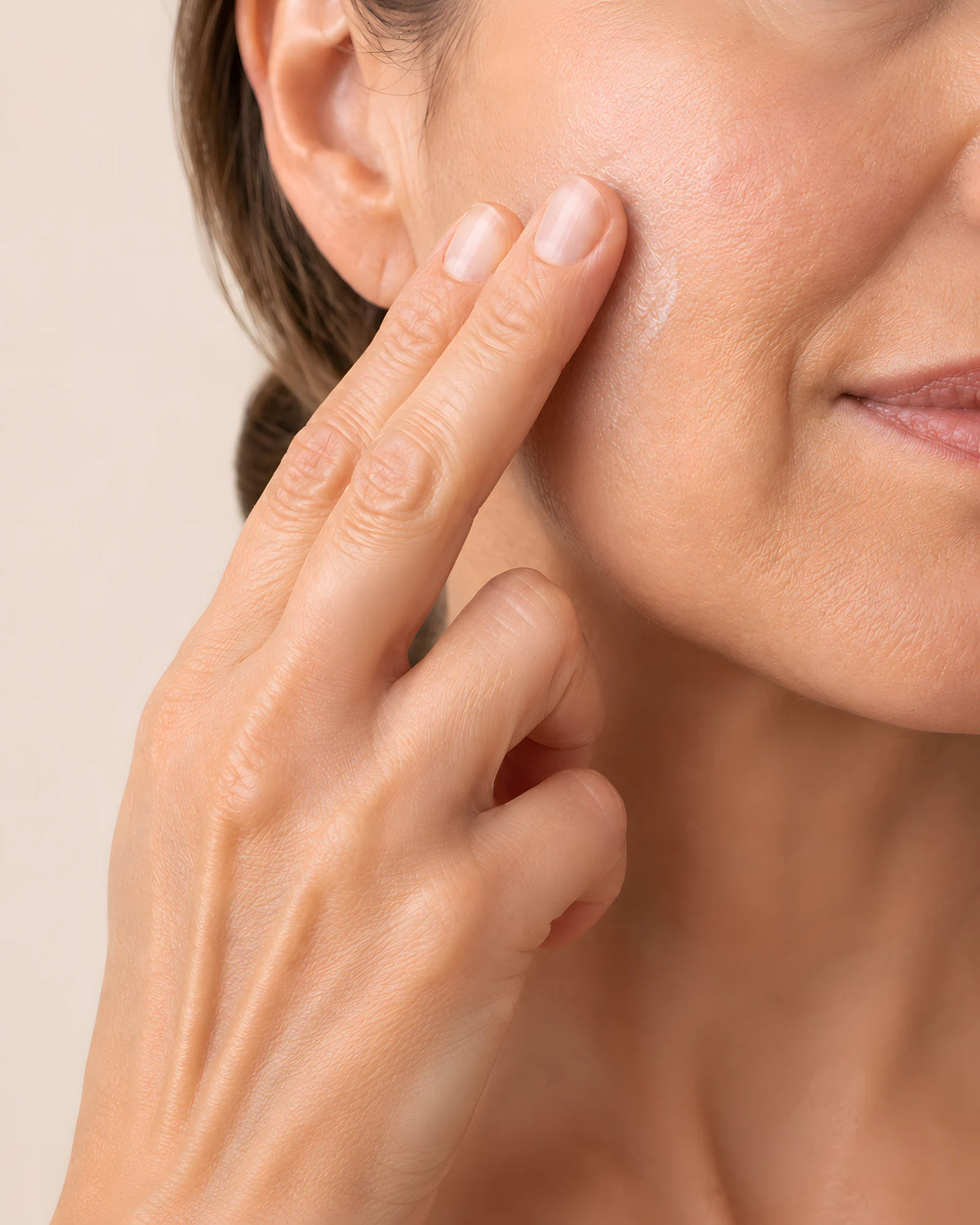 A woman pressing a small amount of the cream onto her cheek with her fingertips